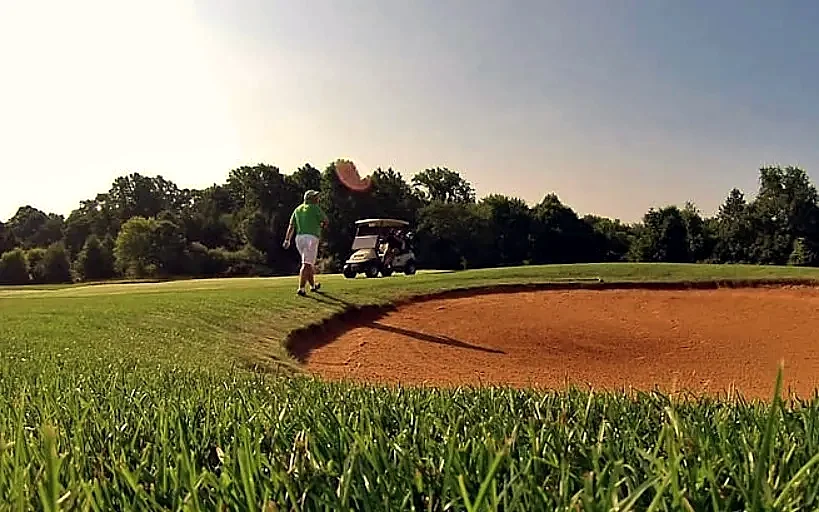 A golfer driving a buggy near a bunker